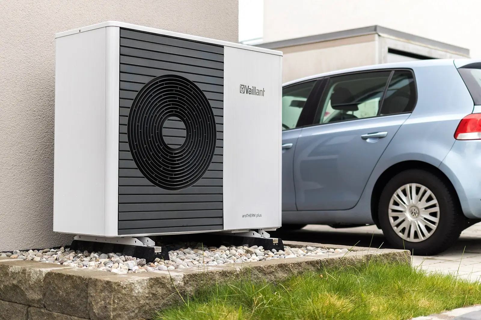 Unité extérieure d’une pompe à chaleur air-eau sur un lit de galets, devant une maison neuve